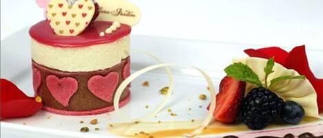 A dessert with a heart-shaped decoration on top, strawberries, and a small chocolate piece.