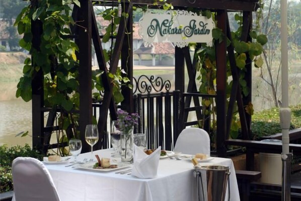 Ein Essbereich im Freien mit einem Tisch für zwei Personen, umgeben von einer Pergola mit Kletterpflanzen.