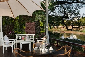 Un espace extérieur aménagé avec une table et des chaises, un parasol blanc et une vue sur un étang.
