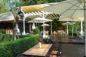 Une terrasse extérieure avec des tables et des parasols, entourée de verdure.