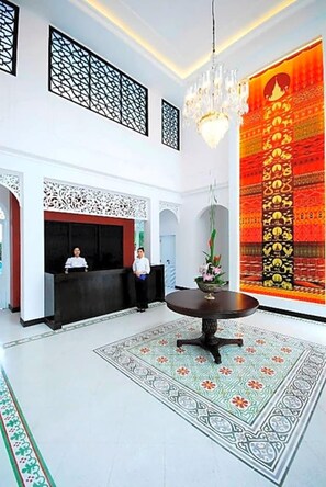 Un vestíbulo de hotel con mostrador de recepción, un candelabro y una gran decoración mural.