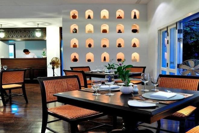 A restaurant with a modern interior, featuring a long dining table with chairs, a wall with recessed lighting, and a view of the outdoors.