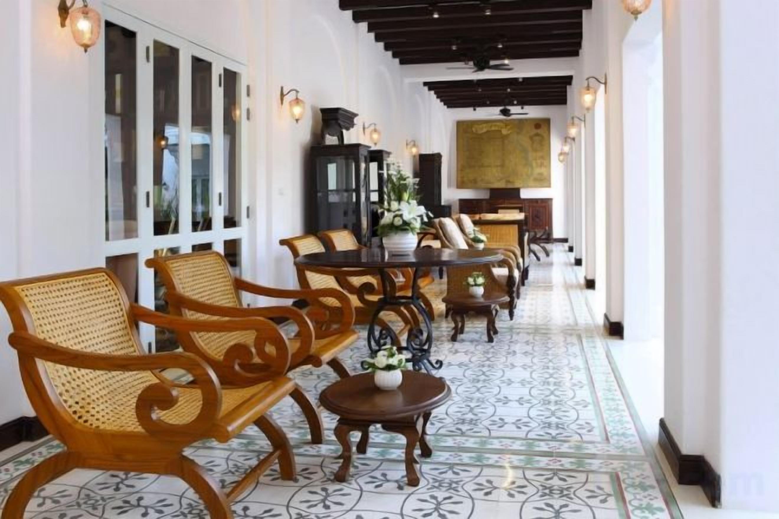 A corridor with wicker chairs and tables, a patterned floor, and wall-mounted lights.
