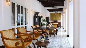 A corridor with wooden chairs and tables, a patterned floor, and wall-mounted lights. - Ping Nakara Boutique Hotel and Spa (Chiang Mai)