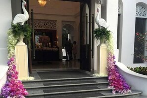 Entrada de hotel con escalones que conducen a la recepción, flanqueada por estatuas blancas y arreglos florales.