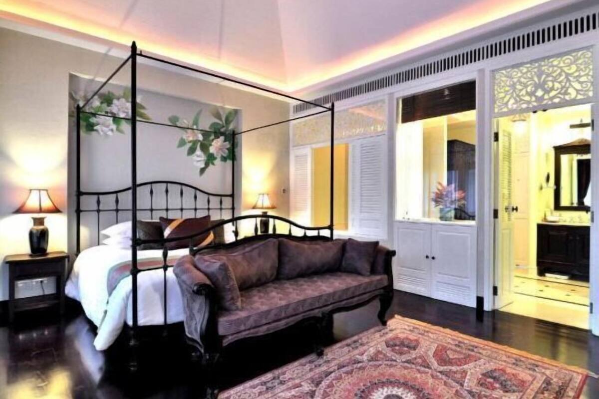 Un dormitorio con cama con dosel, un sofá, un tapete estampado y un adornado en la pared.