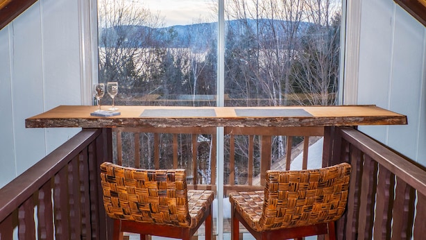 Une terrasse en bois avec une table et deux chaises en osier, une fenêtre donnant sur des arbres et des montagnes, et une pancarte sur laquelle on peut lire : « La vie est belle ».
