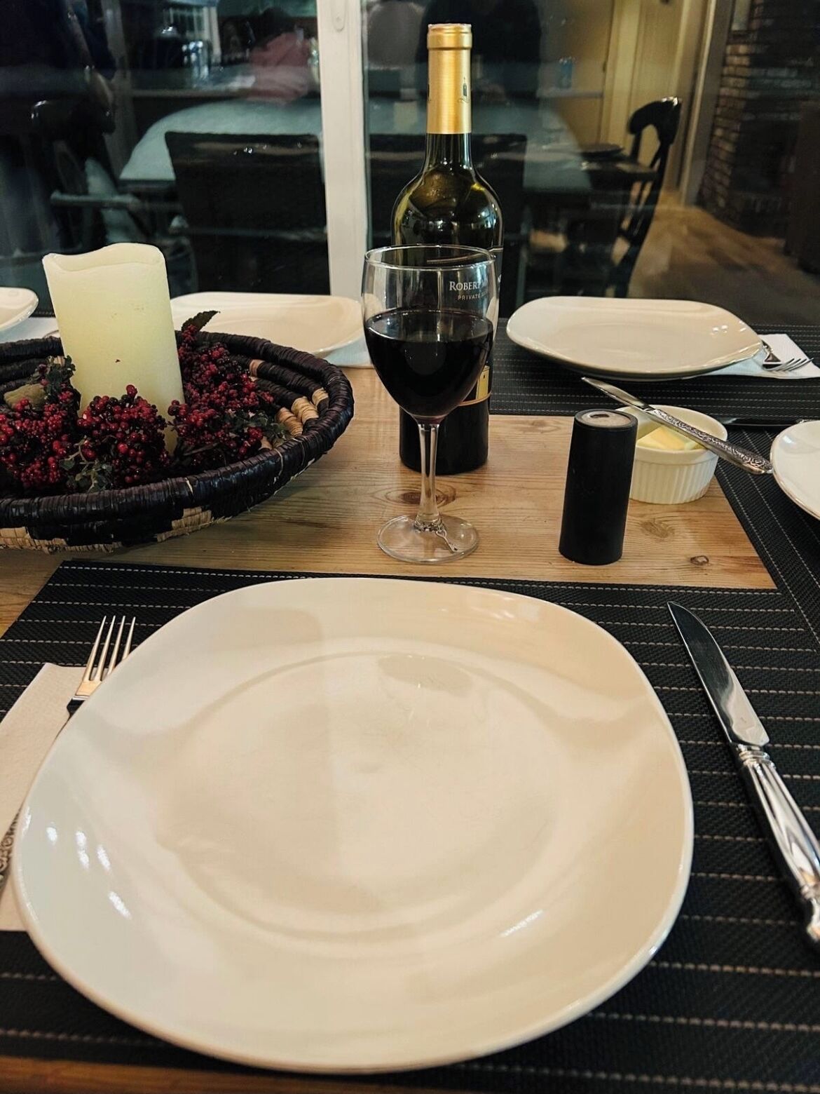 Uma mesa posta com um prato branco, um copo de vinho tinto, uma vela e uma garrafa de vinho.