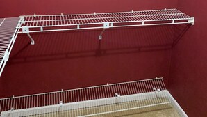 Una habitación con una pared roja, una estantería metálica blanca y suelo cubierto de alfombra.