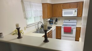 Una cocina con armarios de madera, un microondas, un horno, un fregadero y una ventana con persianas.