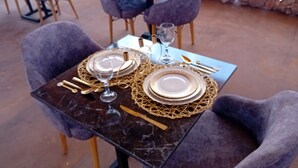 A table set with plates, cutlery, and glasses, surrounded by chairs. - Revolution Stone Cliff Eco Resort  (Agafay)