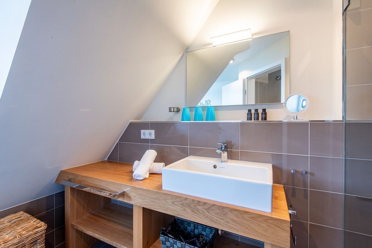 Un baño moderno con tocador de madera, lavabo blanco y espejo arriba.