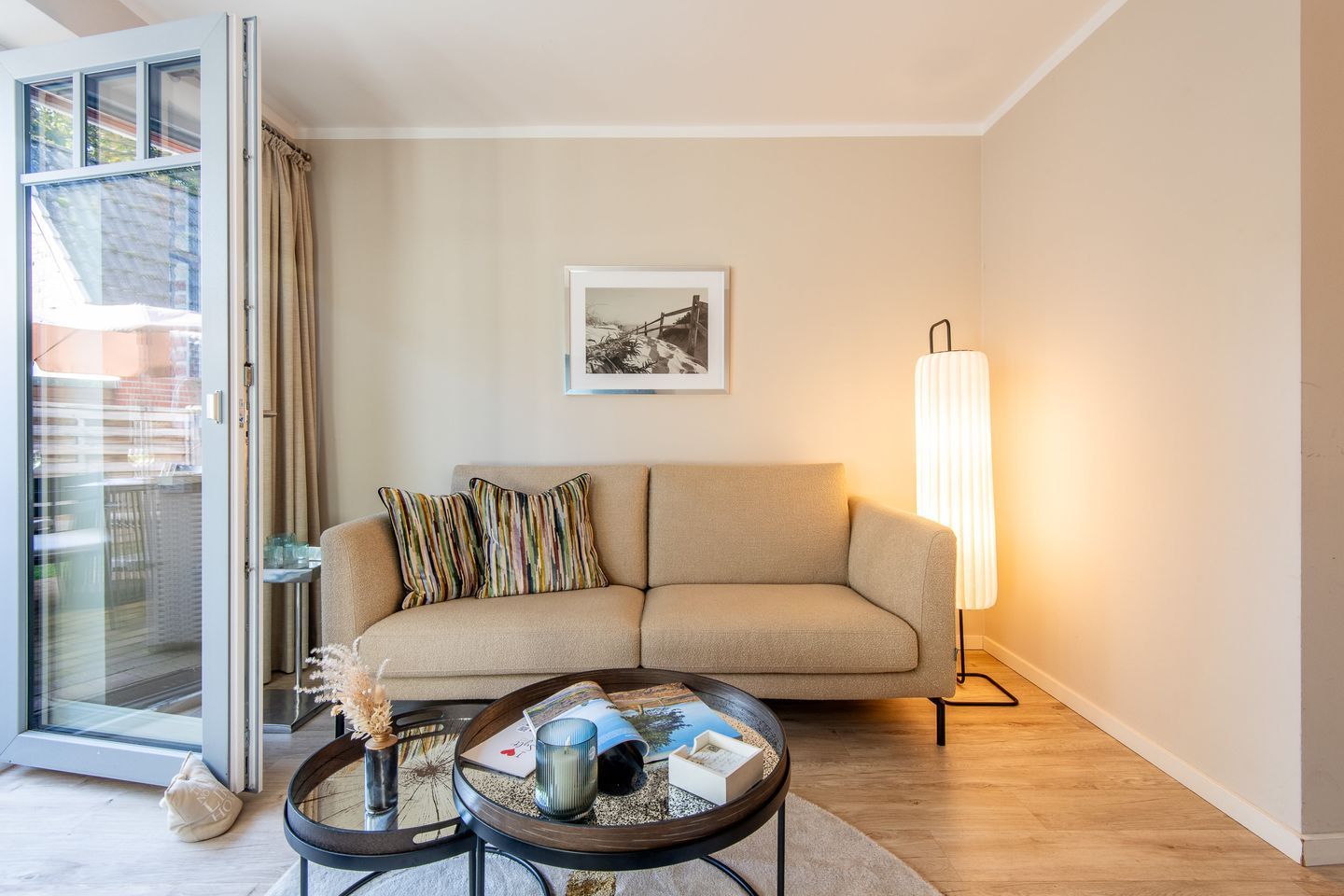 A living room with a sofa, a coffee table, a floor lamp, a framed picture on the wall, and a sliding glass door.