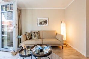 Ein Wohnzimmer mit einer Couch, einem Couchtisch, einer Stehlampe, einem gerahmten Bild an der Wand und einer Schiebetür aus Glas.