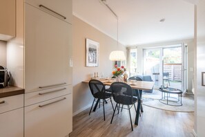 Eine moderne Küche mit weißen Schränken, eine Essecke mit Tisch und Stühlen sowie ein Blick ins Freie durch eine Schiebetür.