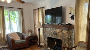 A living room with a stone fireplace, wicker furniture, and a flat-screen TV.