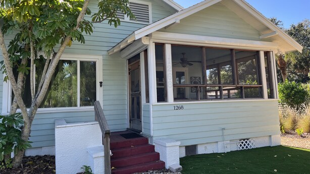 A light green house with a covered porch, a red front door, and a number 1268 on the side.