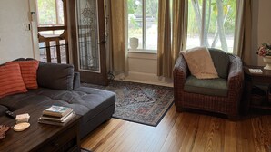 A living room with a dark grey sofa, a wicker chair, and a coffee table with books and a remote control.