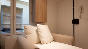 A bedroom with a bed, a wooden wardrobe, a telephone, and a window with blinds. - Charming studio in Versailles - Welkeys (Versailles)