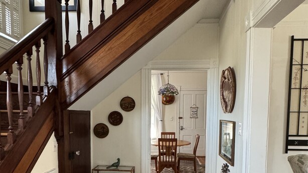 Una escalera con balaustres de madera que conduce a un comedor con un tapete estampado, un banco y una jaula de pájaros.