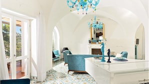 A room with a piano, a chandelier, and a view through a window.