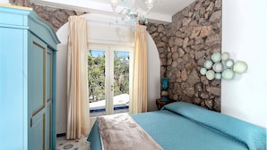 A bedroom with a stone wall, a bed with a blue bedspread, a wardrobe, and a chandelier.