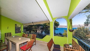 Uma área de estar coberta ao ar livre, com mesa, cadeiras, planta pendente e vista para o mar.