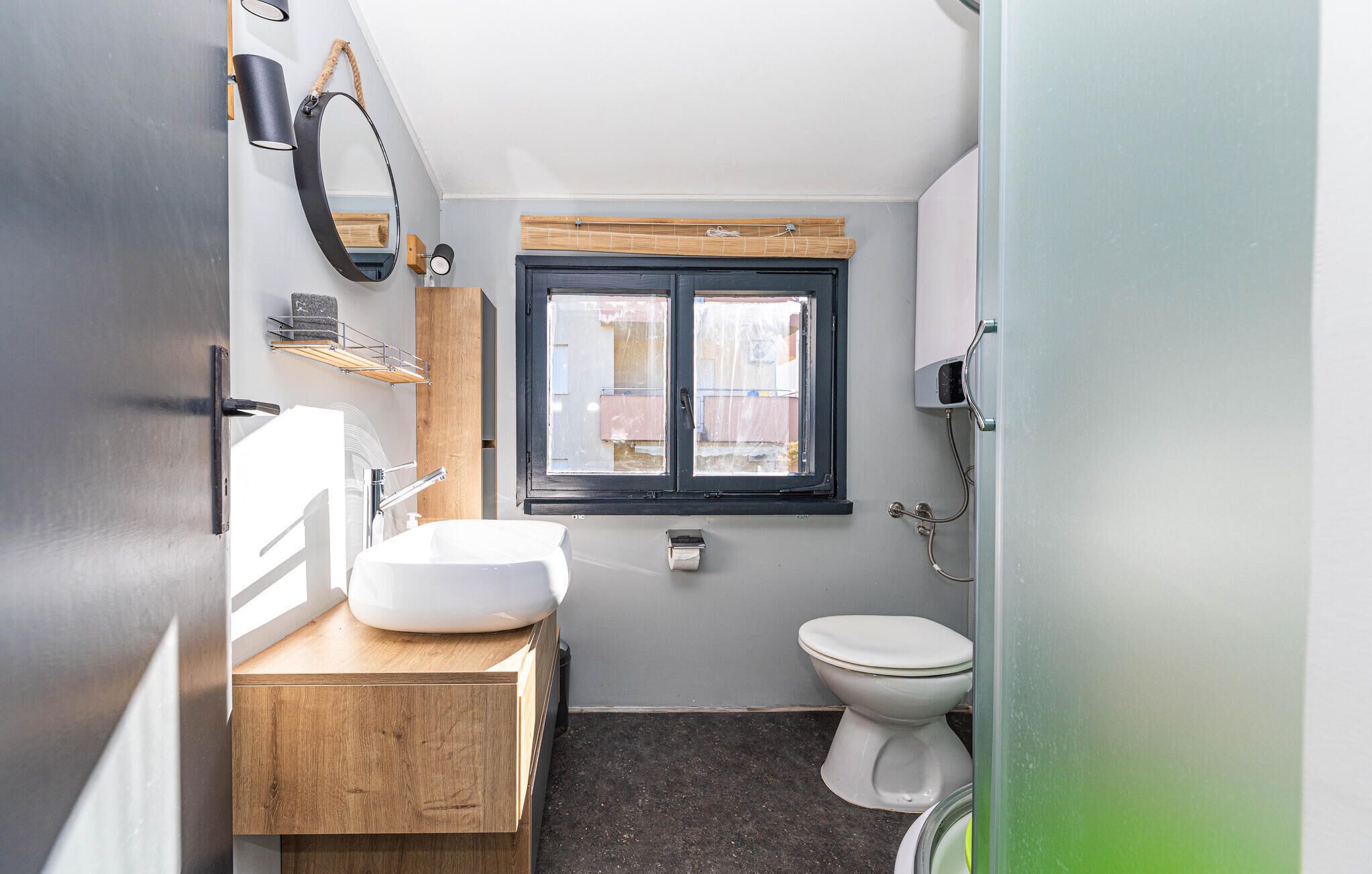 Une petite salle de bain avec un lavabo blanc, un meuble-lavabo en bois, une fenêtre à cadre noir et des toilettes blanches.