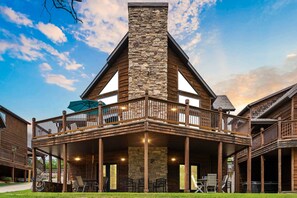 A two-story wooden building with a stone chimney, a balcony with railings, and outdoor seating.
