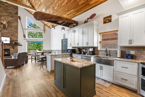 A modern kitchen with white cabinets, a large island, and a stone fireplace.