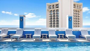 A rooftop pool with lounge chairs and a view of a tall building.