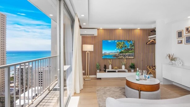 A modern living room with a large window overlooking the ocean, a round coffee table, and a mounted painting.