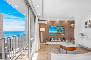 A modern living room with a large window overlooking the ocean, a round coffee table, and a mounted painting.