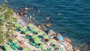 Une plage avec de nombreux parasols verts et blancs à rayures, des chaises longues et des gens qui se baignent dans l’eau.