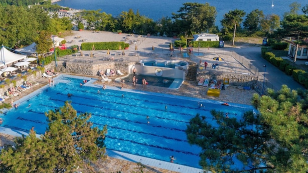 Une piscine dotée de plusieurs couloirs, entourée d’une terrasse en pierre et de parasols, et offrant une vue imprenable sur la côte, la mer et les collines lointaines.