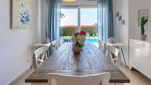A dining area with a wooden table, white chairs, and a vase of flowers. There are two pendant lights above the table. - Augusta by Interhome (Rovinj/Žminj)