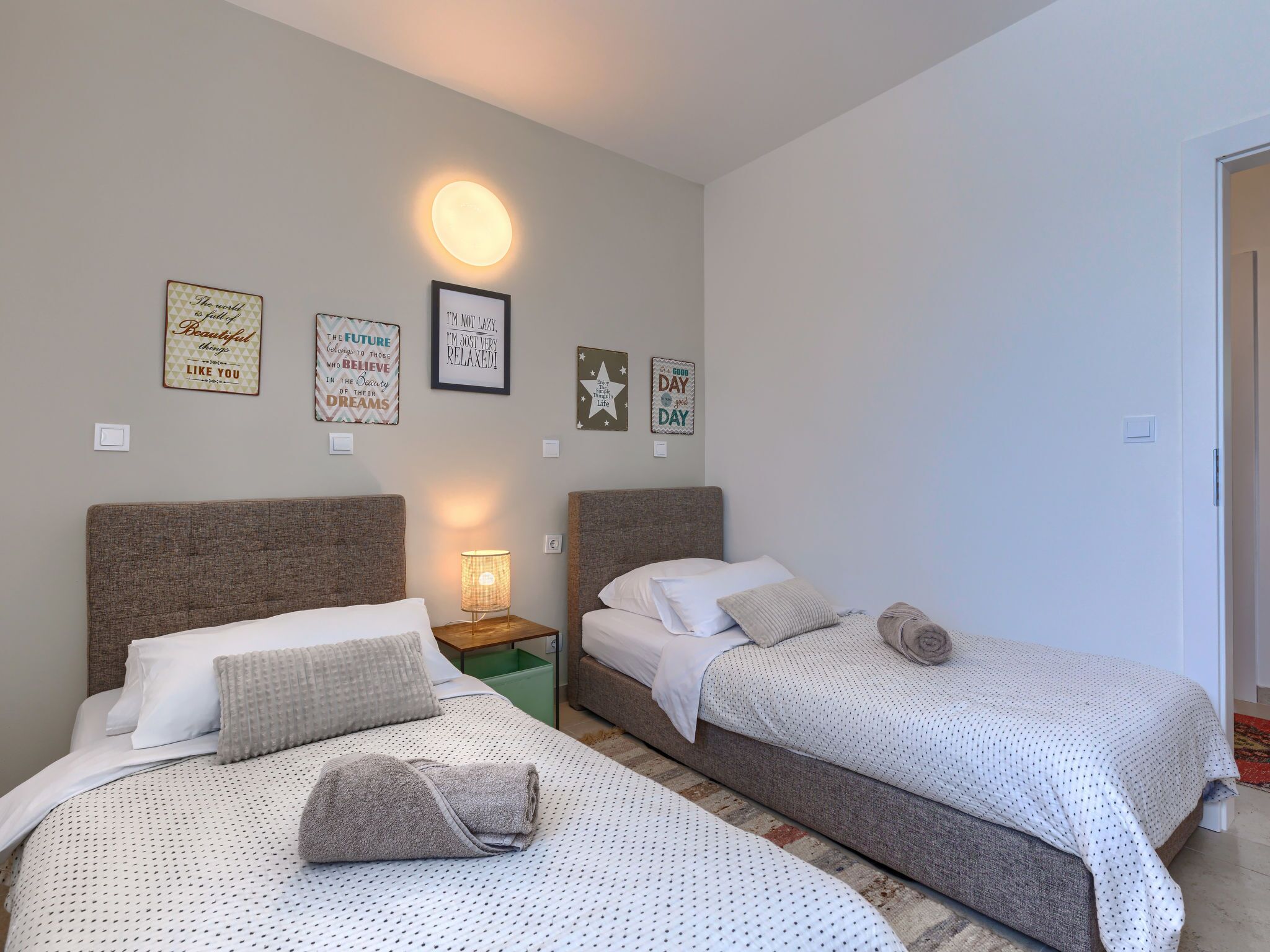 A bedroom with two beds, a nightstand with a lamp, and motivational wall art.