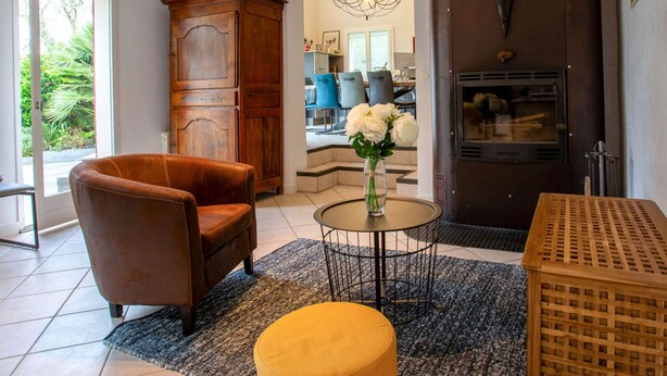 A living room with a brown leather armchair, a round table with a vase of flowers, a wooden cabinet, and a fireplace. - Rive Droite by Interhome (La Bernerie-en Retz)