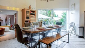 A dining area with a large wooden table, chairs, and a bench. There is a bookshelf and a window with a view of greenery. - Rive Droite by Interhome (La Bernerie-en Retz)