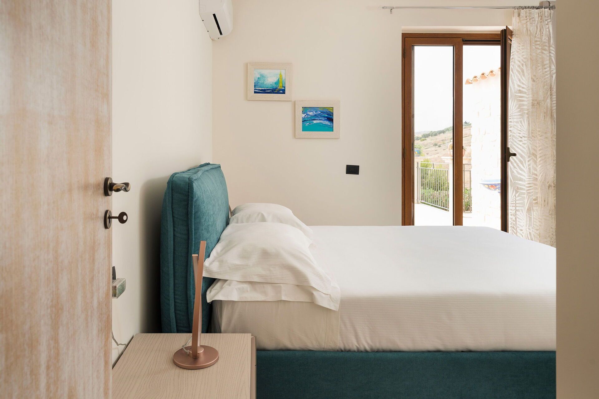 Ein Schlafzimmer mit Bett, Fenster und Blick ins Freie sowie einer Tür.