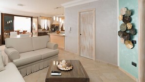 Un soggiorno con divano, tavolino e oggetti decorativi, angolo cottura e parete verde acqua con piatti decorativi.