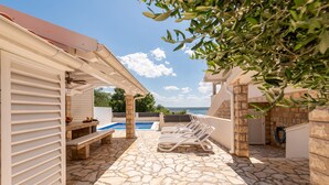 An outdoor patio with a stone floor, a pool, and lounge chairs.