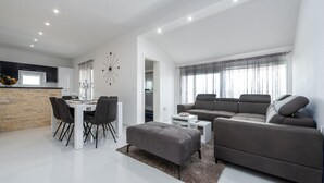 A modern living room with a grey sofa, a dining table with chairs, and a kitchen area with a brick backsplash.