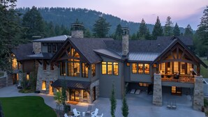 Una casa grande de varios pisos con fachada de piedra, ventanas amplias y un amplio patio exterior con una chimenea y asientos.