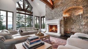 Amplia sala de estar con chimenea de piedra, ventanas grandes y un rincón de estar acogedor.