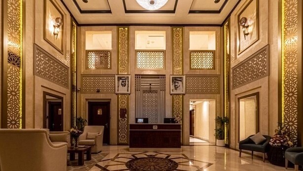 A spacious lobby with a reception desk, seating area, decorative wall panels, and a patterned floor.