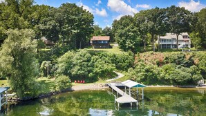 Uma propriedade à beira do lago com um cais, uma galeria coberta e duas casas grandes rodeadas por vegetação densa.