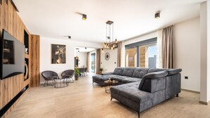 A modern living room with a grey sectional sofa, two armchairs, a coffee table, and a TV mounted on a wooden panel wall. - Lovely home in Miranje Donje (Miranje Donje)