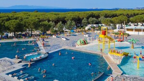 A large outdoor swimming pool area with multiple pools and water play structures, surrounded by trees and beachside amenities.