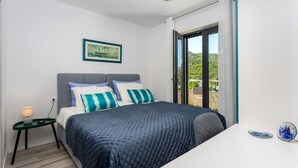 Une chambre à coucher avec un lit, une table de chevet, un tableau encadré et une vue sur un balcon.
